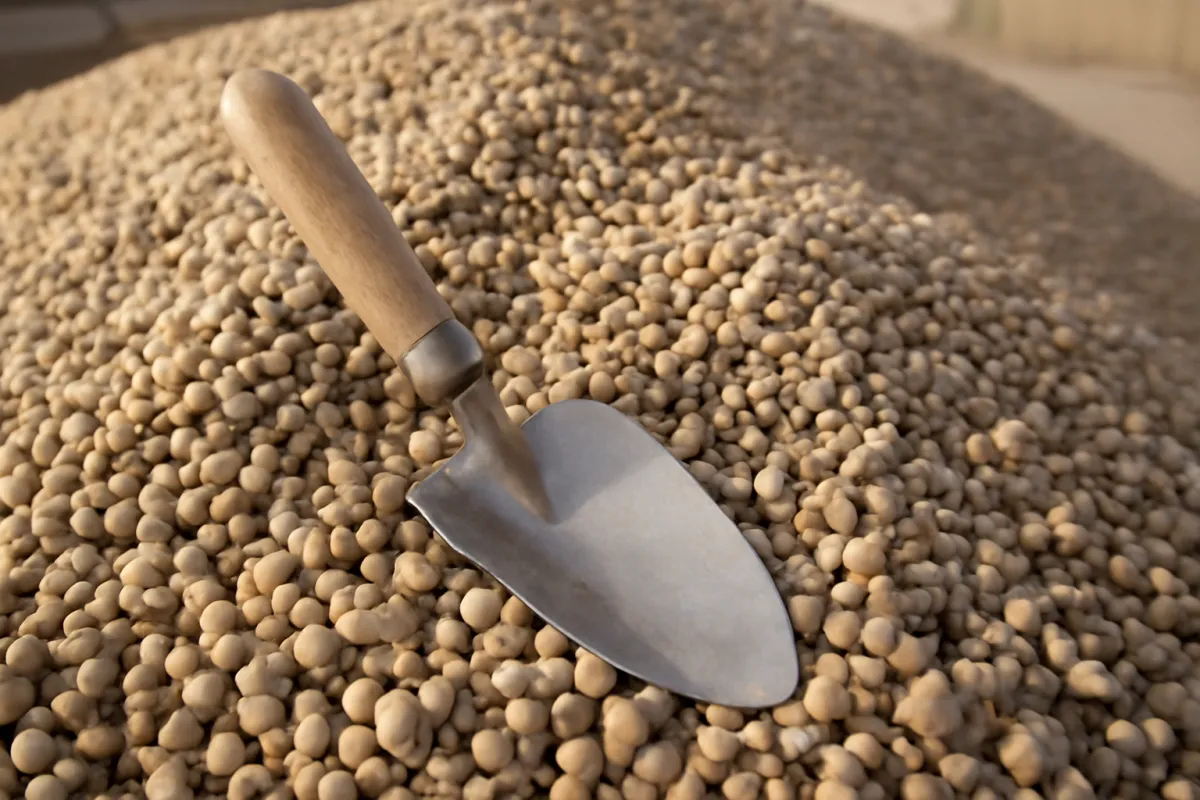 Close-up of a pile of small smooth rounded pea gravel in warm tan and grey tones with a garden trowel resting in it